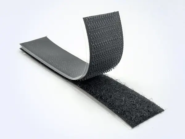Tiras negras de velcro HALCO A8 con revestimiento protector de PET transparente parcialmente despegado para mostrar el adhesivo acrílico.