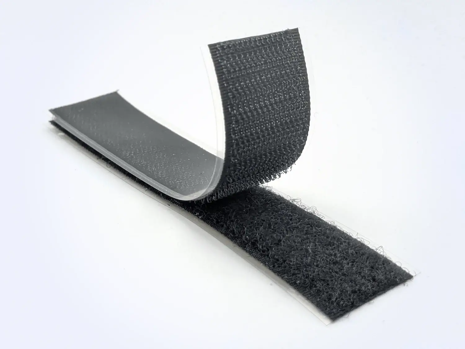 Black HALCO A8 hook and loop strips with clear PET release liners partially peeled back to show the acrylic adhesive backing.