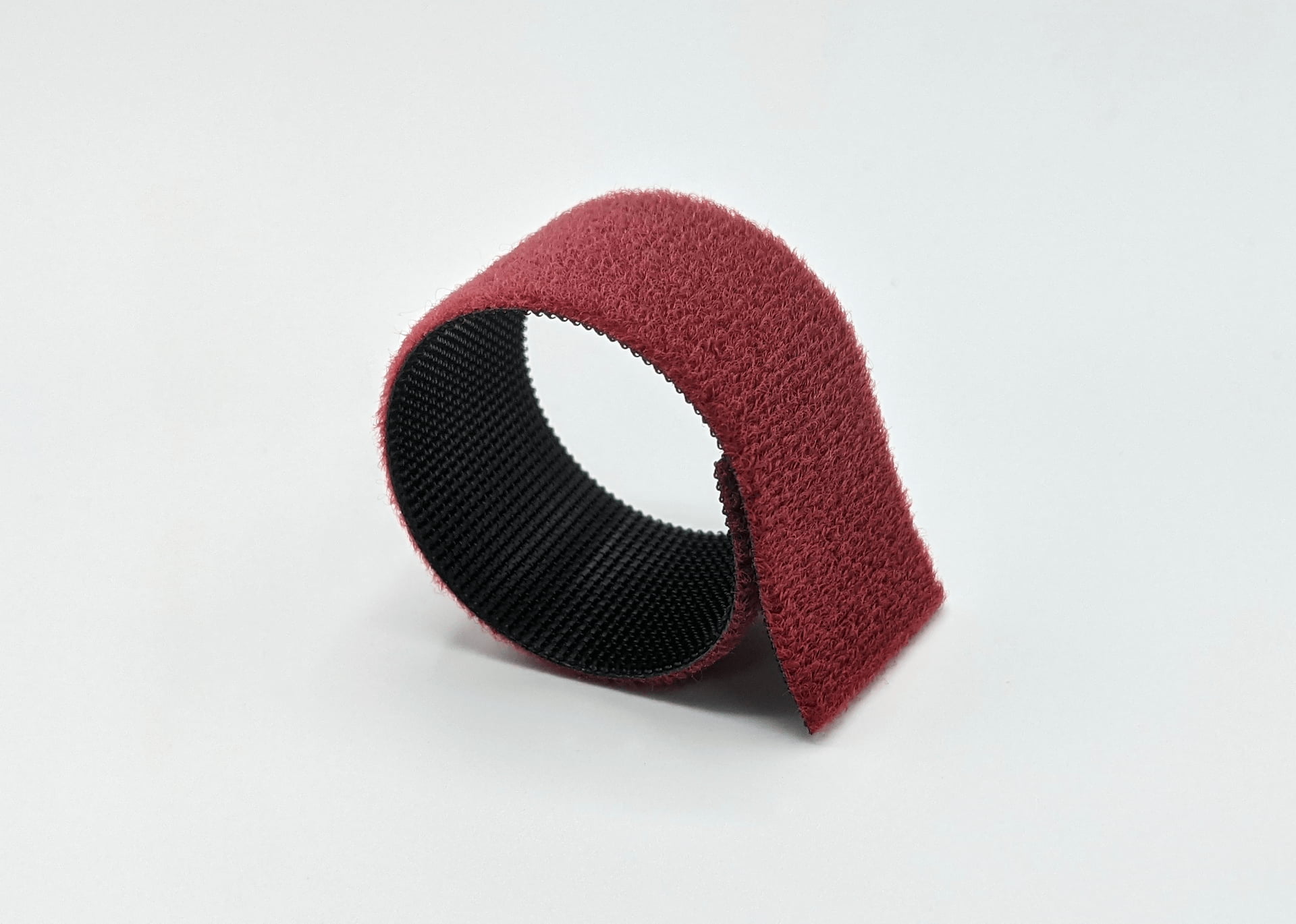 Upright red hook and loop strap, one end draped over itself, exposing a black textured inner side.